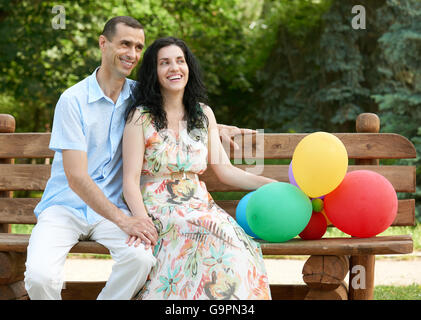 Romantisches Brautpaar mit Ballon sitzen auf Bank im Stadtpark und posiert, Sommersaison, Erwachsene Personen Mann und Frau Stockfoto