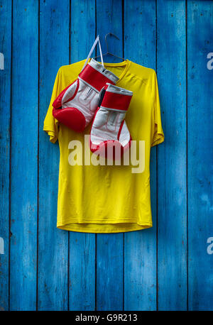 Gelbes T-shirt und Boxhandschuhe an einer hölzernen alten blauen Wand hängen Stockfoto