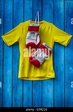 Gelbes T-shirt und Boxhandschuhe an einer hölzernen alten blauen Wand hängen Stockfoto