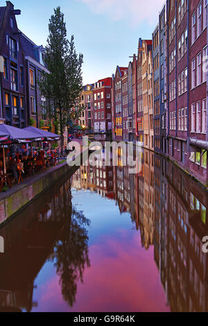 Häuser und Restaurants am Oudezijds Achterburgwal Kanal bei Sonnenuntergang in Amsterdam, Holland Stockfoto
