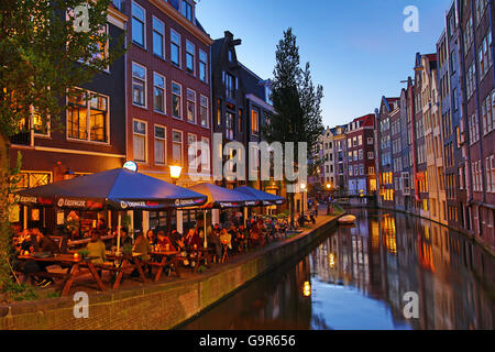 Häuser und Restaurants am Oudezijds Achterburgwal Kanal bei Sonnenuntergang in Amsterdam, Holland Stockfoto