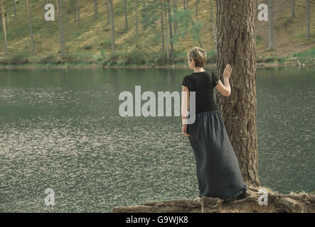 einsame junge Frau im langen Rock stehen am Ufer des Sees und Blicke in Ferne Stockfoto