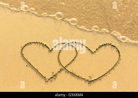 Zwei Herzen auf einem sandigen goldenen Strand von Hand gezeichnet. Stockfoto