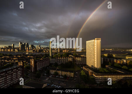 London, UK. 1. Juli 2016. UK Wetter: Bunte Regenbogen bricht während einer kurzen Abend Gewitter über Süd-Ost-London, inklusive ein Hochhaus Sozialsiedlung Gebäude (rechts) und Canary Wharf Business Park Gebäude (links) Credit: Guy Corbishley/Alamy Live News Stockfoto