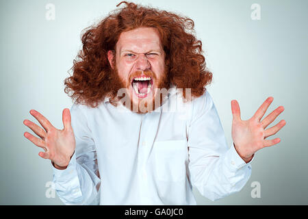 Porträt von kreischenden jungen Mann mit langen roten Haaren und schockiert Gesichtsausdruck auf grauem Hintergrund Stockfoto