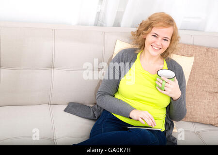 Eine junge plus Größe Frau mit einem Tablet-PC auf einem Sofa sitzt. Stockfoto