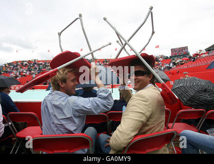 Fans nutzen Stühle, um sich während der Artois Championships im Queen's Club, London, vor dem Regen zu schützen. Stockfoto