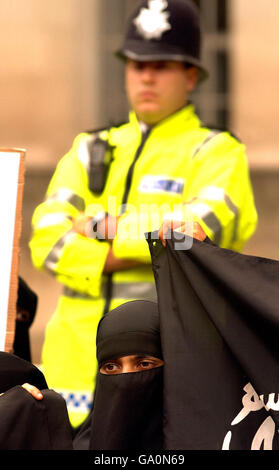 Ein Polizeibeamter steht hinter einer großen Gruppe von muslimen, die gegen die britische Regierung gegenüber dem Eingang zur Downing Street im Zentrum von London demonstrieren. Stockfoto