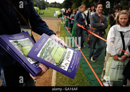 Schlangen warten im Trockenen, um ihre Armbänder für den Mittelplatz zu erhalten, während ein Programmverkäufer während der All England Lawn Tennis Championship in Wimbledon an der Reihe ist. Stockfoto