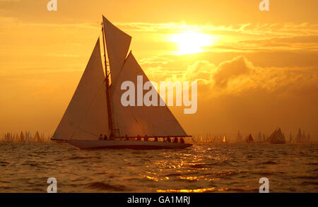 Die Sonne geht auf, als Kelpie, ein 1903 Solent One Design Gaff, zu Beginn des JP Morgan Round the Island Race von der Startlinie in Cowes, Isle of Wight, rast. Der Start wurde um 5 Uhr vorangebracht, nachdem einige Boote letztes Jahr die Flut nicht überstanden hatten und an den Needles festsaßen. Stockfoto