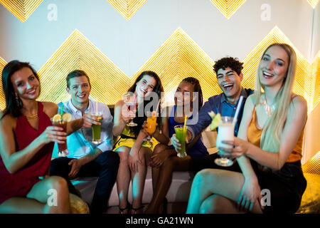 Gruppe von lächelnden Freunde auf Sofa sitzen und ein Glas Cocktail zeigt Stockfoto