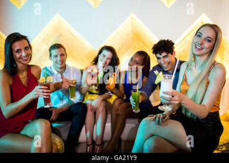 Gruppe von lächelnden Freunde auf Sofa sitzen und ein Glas Cocktail zeigt Stockfoto