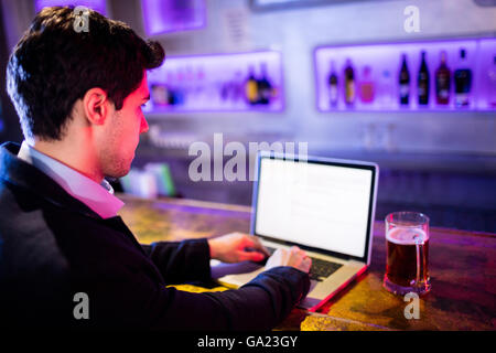 Mann mit Laptop mit Glas Bier am Tisch am Tresen Stockfoto