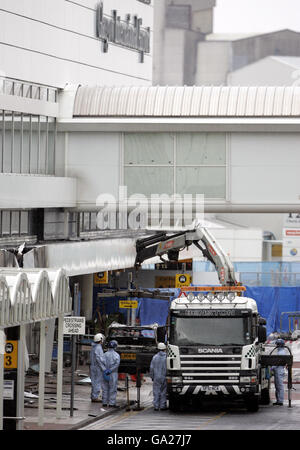 Forensische Polizeibeamte sehen sich an, als das Wrack des Jeep Cherokee vom Schauplatz des gestrigen dramatischen Angriffs auf das Terminalgebäude am Flughafen Glasgow entfernt wird. Stockfoto