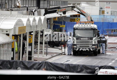 Forensische Polizeibeamte sehen sich an, als das Wrack des Jeep Cherokee vom Schauplatz des gestrigen dramatischen Angriffs auf das Terminalgebäude am Flughafen Glasgow entfernt wird. Stockfoto