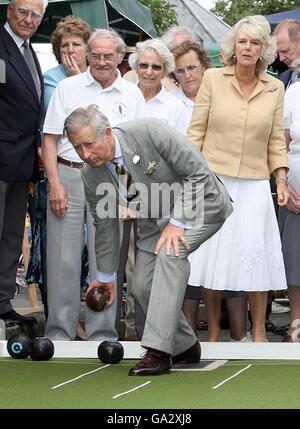 Der britische Prinz Charles, der Prinz von Wales, versucht sich beim Bowling, während seine Frau Camilla, Herzogin von Cornwall, bei einem Besuch im Dorf Bromham in Wiltshire zuschaut. Stockfoto