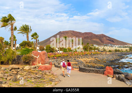 Paar Touristen zu Fuß auf Küstenpromenade entlang Meer in Playa Blanca, Lanzarote, Kanarische Inseln, Spanien Stockfoto