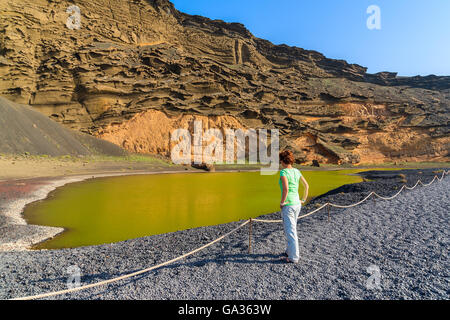 Junge Frau Touristen stehen durch das grüne Wasser des Lago Verde, El Golfo, Lanzarote, Kanarische Inseln, Spanien Stockfoto