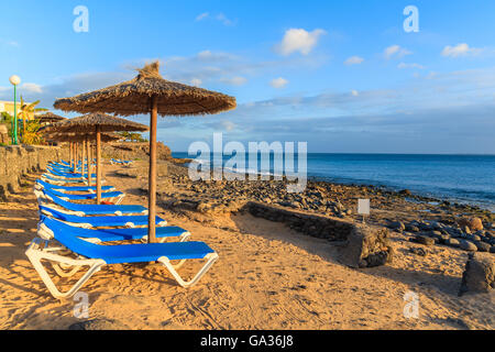 Reihe von Liegestühlen und Sonnenschirmen am Strand von Playa Blanca bei Sonnenuntergang, Lanzarote, Kanarische Inseln, Spanien Stockfoto