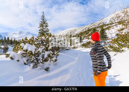 Junge Frau Tourist in Pullover, orange Hose und roten Hut Winter Weg im Gasienicowa Tal, Tatra-Gebirge, Polen Stockfoto