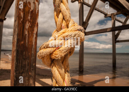 Nahaufnahme von einem dicken orange farbigen verknoteten Seil hängend von einem Pier an einem Strand in Hartlepool im Nordosten von England Stockfoto
