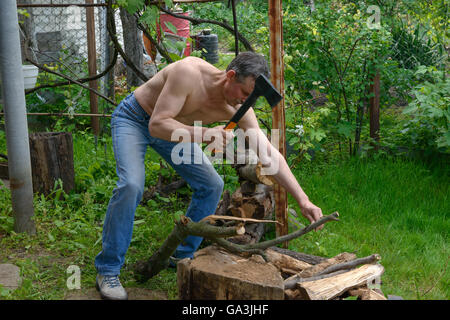 Muskulärer reifer Mann ist Zweig auf Holz-Block von Axe auf dem Hinterhof hewing. Stockfoto