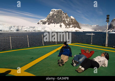 Touristen, die auf dem Hubschrauberlandeplatz des Antarctic Dream entspannende versenden, Lemaire-Kanal, antarktische Halbinsel, Antarktis Stockfoto