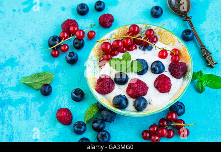 Frischen Joghurt mit Himbeeren, Heidelbeeren und roten Johannisbeeren in einer Schüssel mit Minze Blätter auf lackiertem Holz Stockfoto