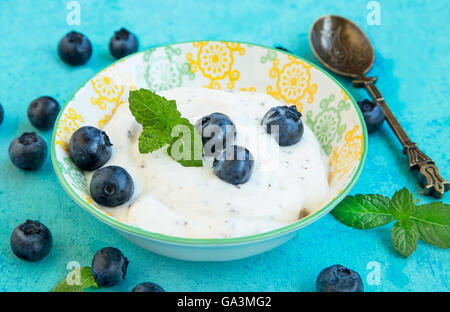 Frischen Joghurt mit Blaubeeren und Minze Blätter in rustikalen Schüssel auf lackiertem Holz Stockfoto