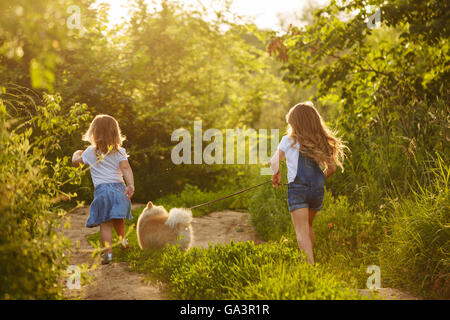 Kleine Schwestern und Haustier. Mädchen und Hund zu Fuß entlang der Straße im Stadtpark. Rassehunde Spitz. Gehen Sie weg. Stockfoto