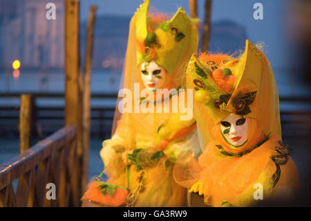 Masketeers in aufwendigen dekorativen gelben Kostüm posiert auf dem Holzsteg durch den Canal Grande in Venedig Maske Festival Stockfoto