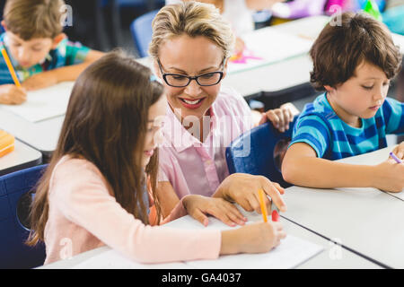 Lehrer hilft Mädchen bei den Hausaufgaben im Klassenzimmer Stockfoto
