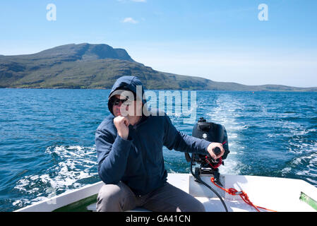 Junger Mann in einem Boot mit Außenbordmotor, schottischen Highlands, UK. Stockfoto