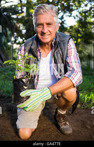 Porträt von glücklich Gärtner kniend mit Topfpflanze im Garten Stockfoto