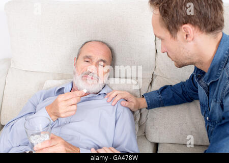 Älterer Mann jüngeren Mann etwas Medizin erhalten, beim liegen auf dem Sofa im Wohnzimmer Stockfoto