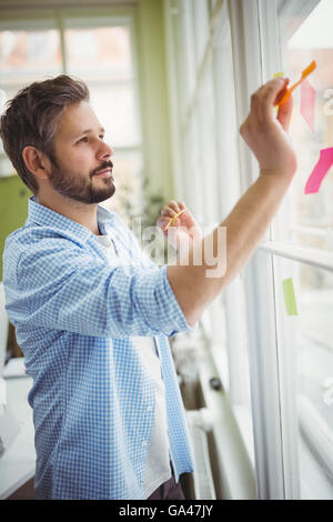 Geschäftsmann kleben Klebefuge Notizen auf Fenster am Kreativbüro Stockfoto