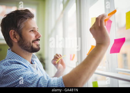 Glücklich Kaufmann kleben Klebefuge Notizen auf Fenster im Büro Stockfoto