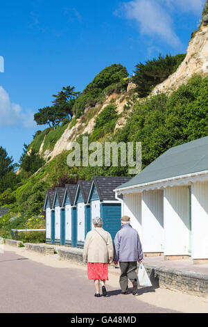 Älteres Ehepaar zu Fuß entlang der Promenade Vergangenheit Strandhütten in Poole, Dorset im Juli Stockfoto