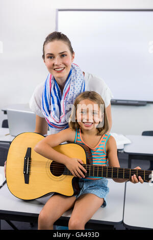 Porträt des Lehrers unterstützen Mädchen Gitarrespielen im Klassenzimmer Stockfoto