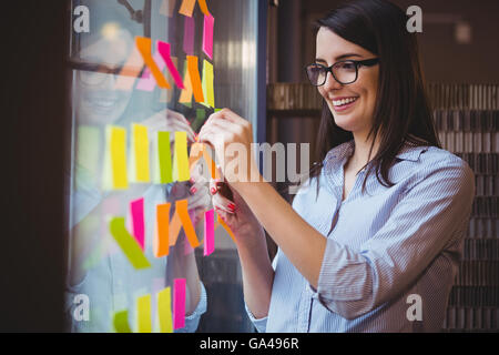 Kreative Geschäftsfrau kleben Klebefuge Notizen im Büro Glas Stockfoto