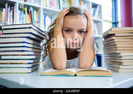 Betonte Mädchen mit Büchern am Tisch in der Schulbibliothek Stockfoto