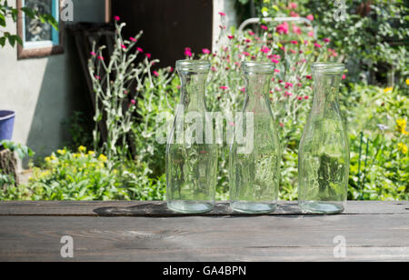 Drei leere Glasflaschen auf einem dunklen Brett auf einem Garten Hintergrund Stockfoto