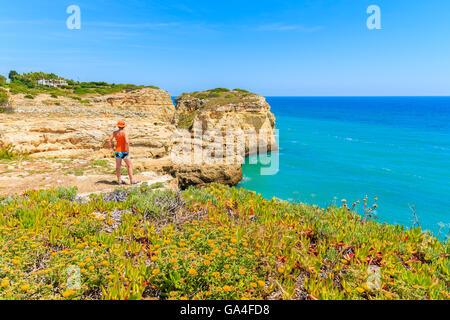 Frühlingsblumen im Vordergrund mit junge Frau Tourist auf Klippe Felsen steht und mit Blick auf Meer, Portugal Stockfoto