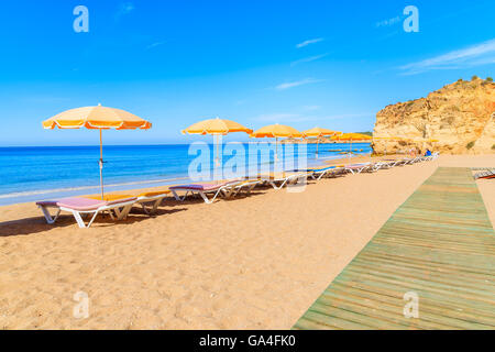 Pfad und Sonnenschirme mit liegen am Strand von Praia da Rocha, Region Algarve, Portugal Stockfoto