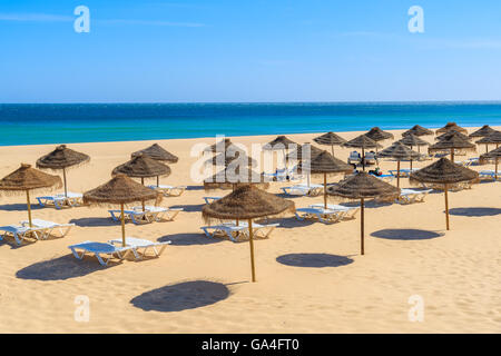 Sonnenschirme mit liegen am goldenen Sandstrand in der Stadt Salema, Portugal Stockfoto