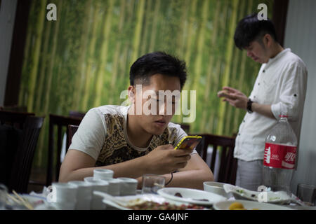 Chinesische Jugendliche spielen mit ihren Smartphones und soziale Netzwerke nach einer Mahlzeit, in Peking, China Stockfoto