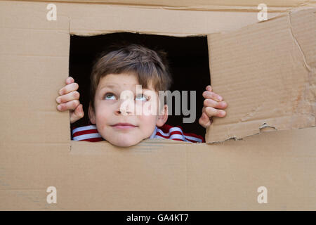 Ein 7 Jahre alter Junge schaut aus dem Fenster aus einem Karton geschnitten Stockfoto