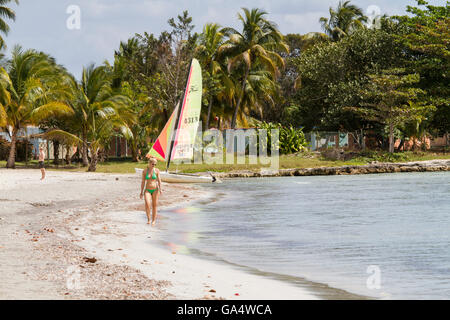 Frau im Bikini zu Fuß am Strand, mit Hobie Cat und Mann im Hintergrund, am Playa Larga, Kuba Stockfoto