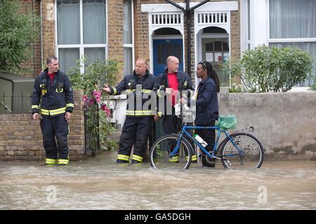 London, UK. 3. Juli 2016. Defekte Wasserleitung verursacht schweren Überschwemmungen in South Wimbledon, London, UK 03.07.2016 Feuerwehren raten einen Radfahrer die sicherste Route außerhalb Reihenhäuser auf Kingston Road steigender Wasserstände aufgrund einer gebrochenen Hauptwasserleitung in South Wimbledon. Bildnachweis: Jeff Gilbert/Alamy Live-Nachrichten Stockfoto