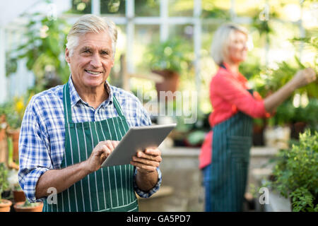 Senior woman mit digital-Tablette während Frau arbeitet im Gewächshaus Stockfoto